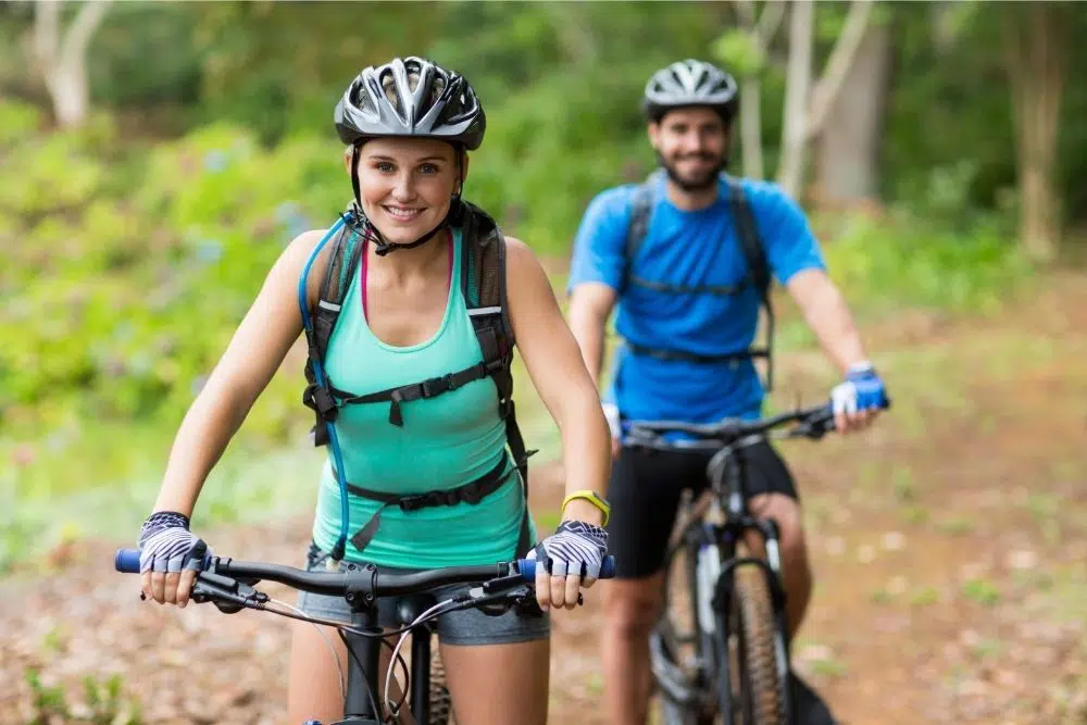 Does cycling burn belly fat? A couple riding their bikes along a forest trail, enjoying an active outdoor workout.