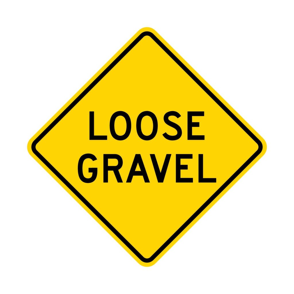 Loose gravel warning road sign with gravel debris visible on road surface illustrating cycling safety sign hazards